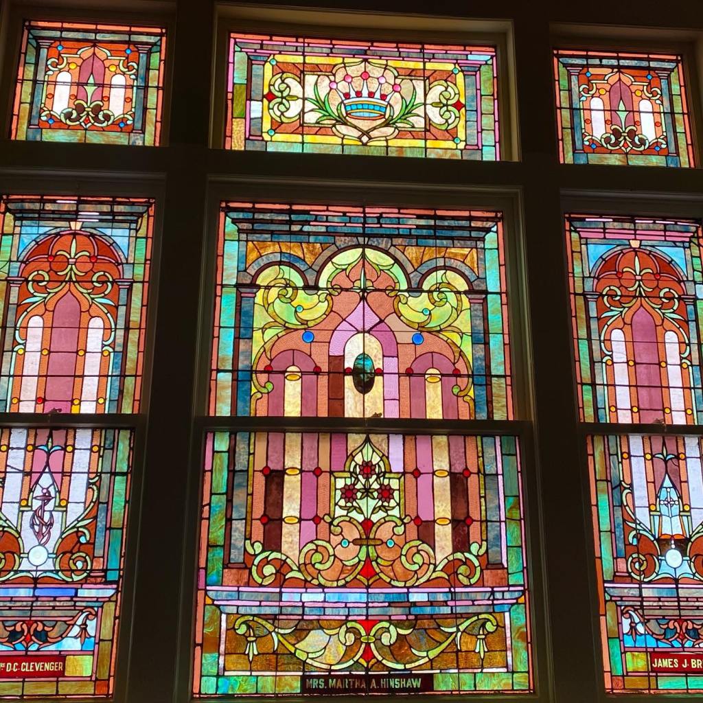 A photo of a wall of rectangular stained glass windows. They are primarily pink, blue, yellow, green, orange, and red.